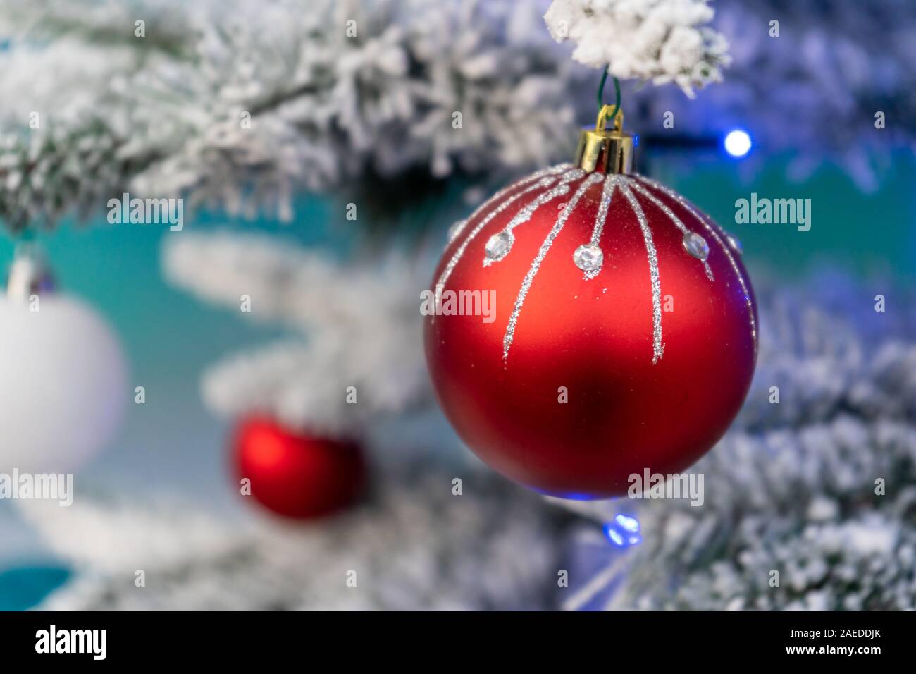 Eine rote Weihnachtskugel mit Glitzer hängen an einem frostigen Weihnachtsbaum Stockfoto