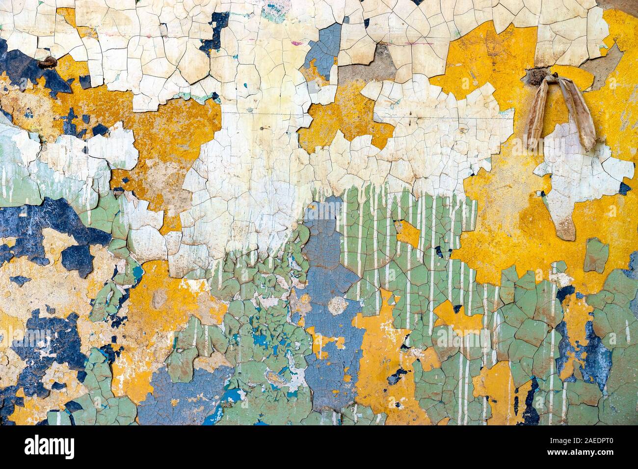 Alte beschädigte Wand mit vielen verschiedenen Schichten von Farbe. Auf der oberen rechten Wand ist ein alter Nagel mit einem Kunststoff band Stockfoto