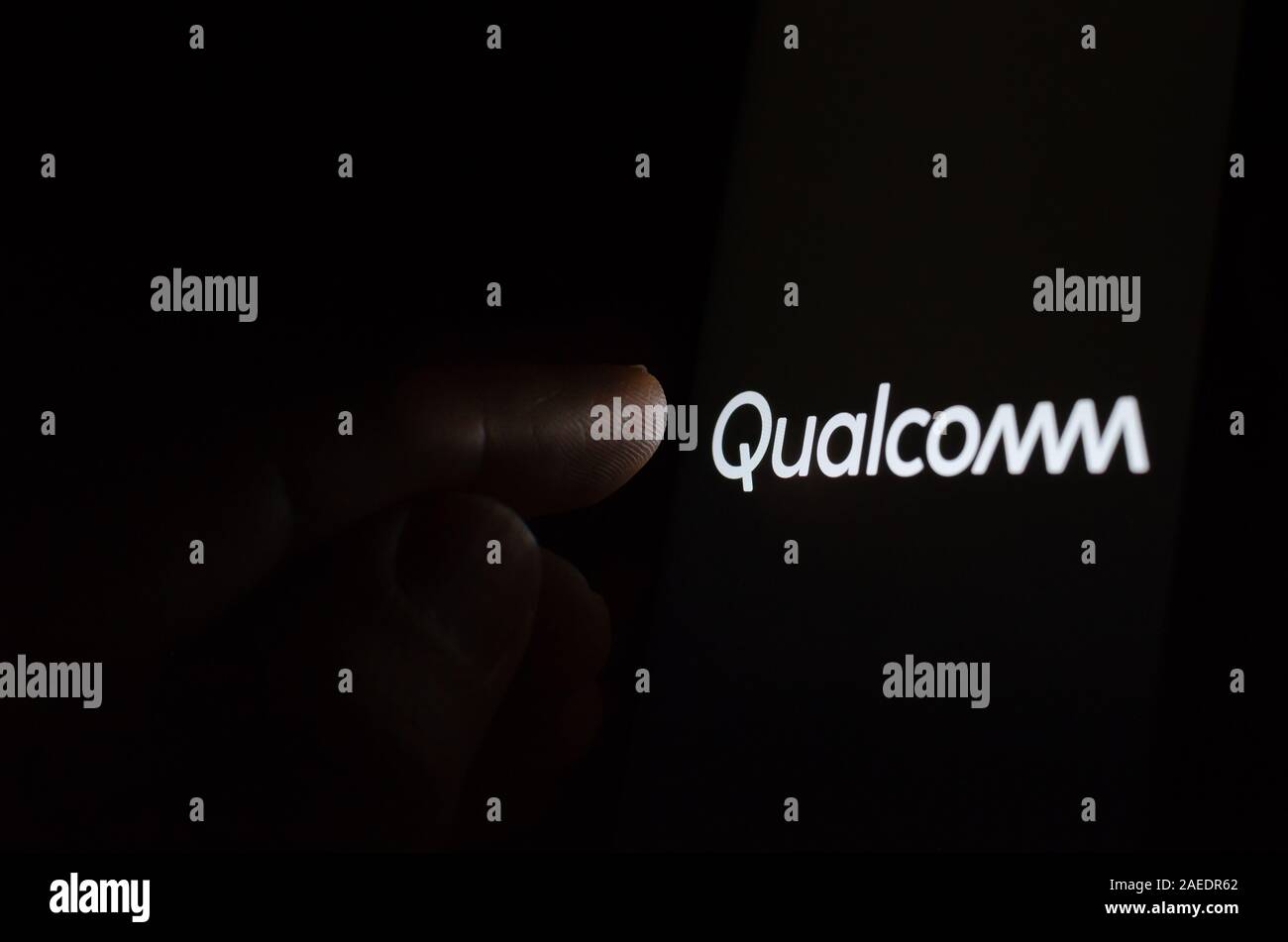 Qualcomm Logo auf einem leuchtenden Bildschirm und eine Hand auf ihn gerichtet. Stockfoto