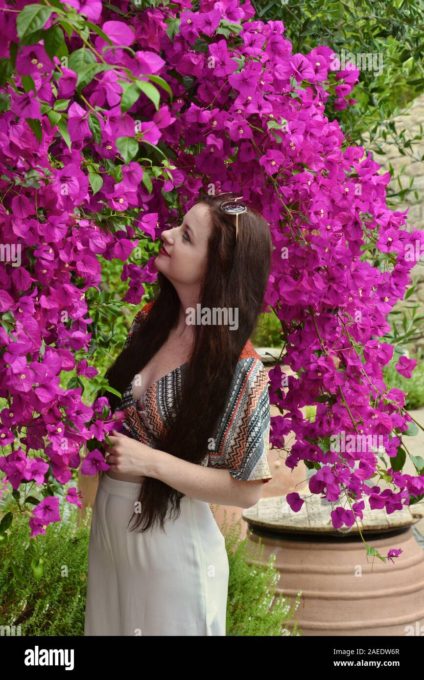 Lange Haare, brünett kaukasischen jungen Dame glücklich unter einem Baum in hell lila Blüten bedeckt Posing, bewundern Sie die Blumen, wie sie nach unten hängen, Drapieren Stockfoto