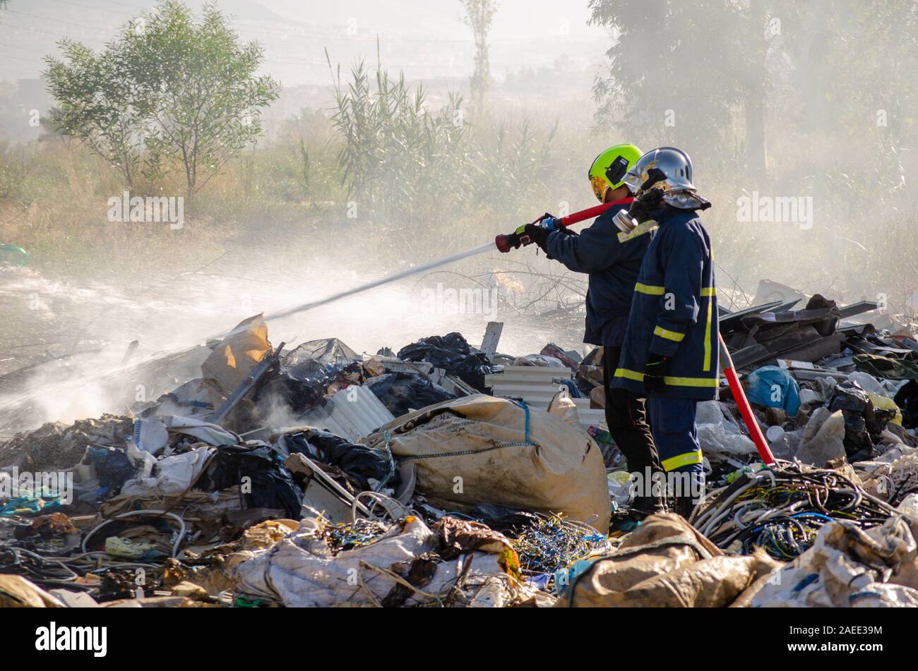 Menidi, Athen/Griechenland am 18. Dezember 2019: illegal Bereiche, Feuerwehrleute begießen, brennende Müll deponie, die giftige Verunreinigung Krise trägt Stockfoto