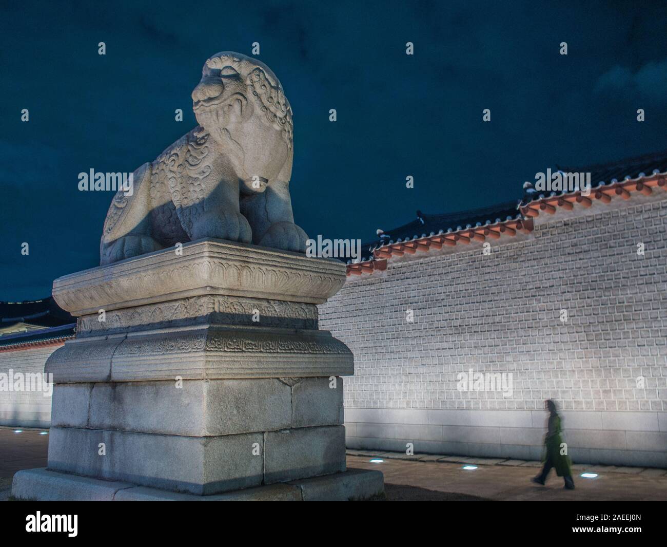 Person zu Fuß vorbei an Wand und riesige Statue, shishi Lion dog Guardian, außerhalb Gyeongbokgung Palast, night street, Seoul, Südkorea Stockfoto