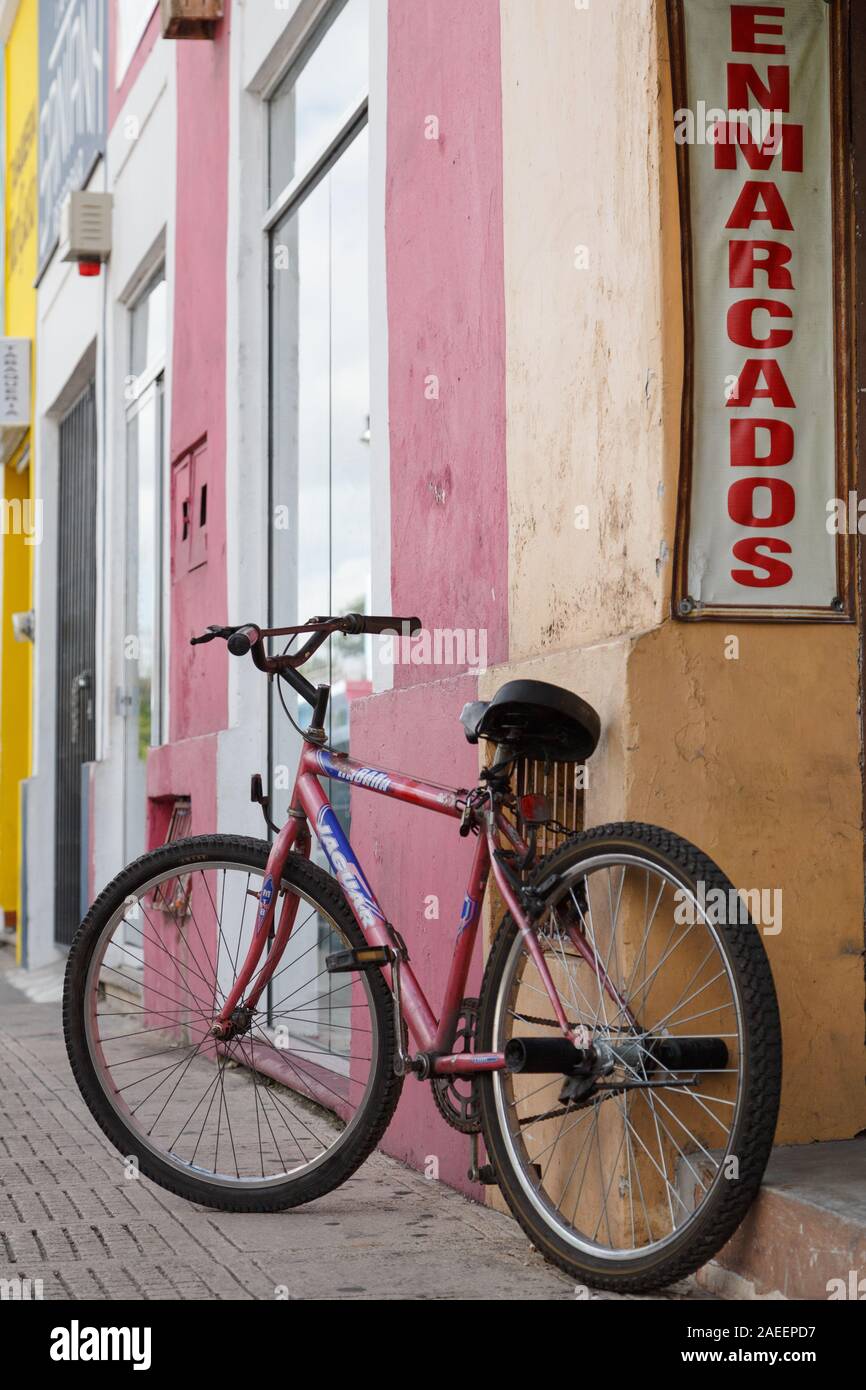 Ein rotes Fahrrad beiläufig durch die bunten Gebäude in der malerischen Bürgersteig von Merida, Yucatan, Mexiko geparkt. Stockfoto