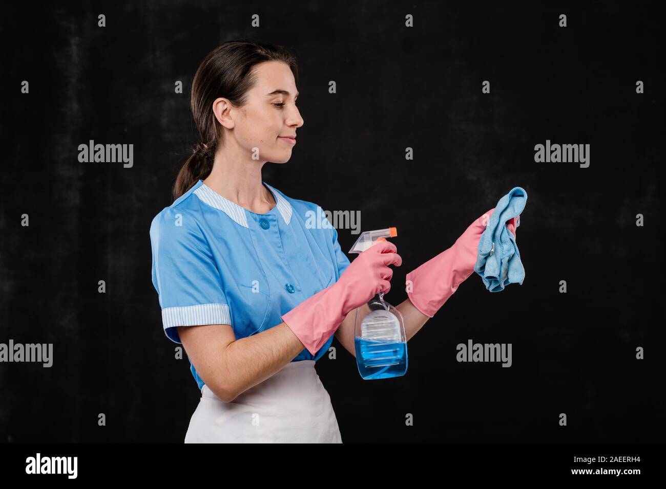 Hübsches Hotel Zimmermädchen in Unifor und rosa Gummi Handschuhe spritzen Reinigungsmittel für den Duster Stockfoto
