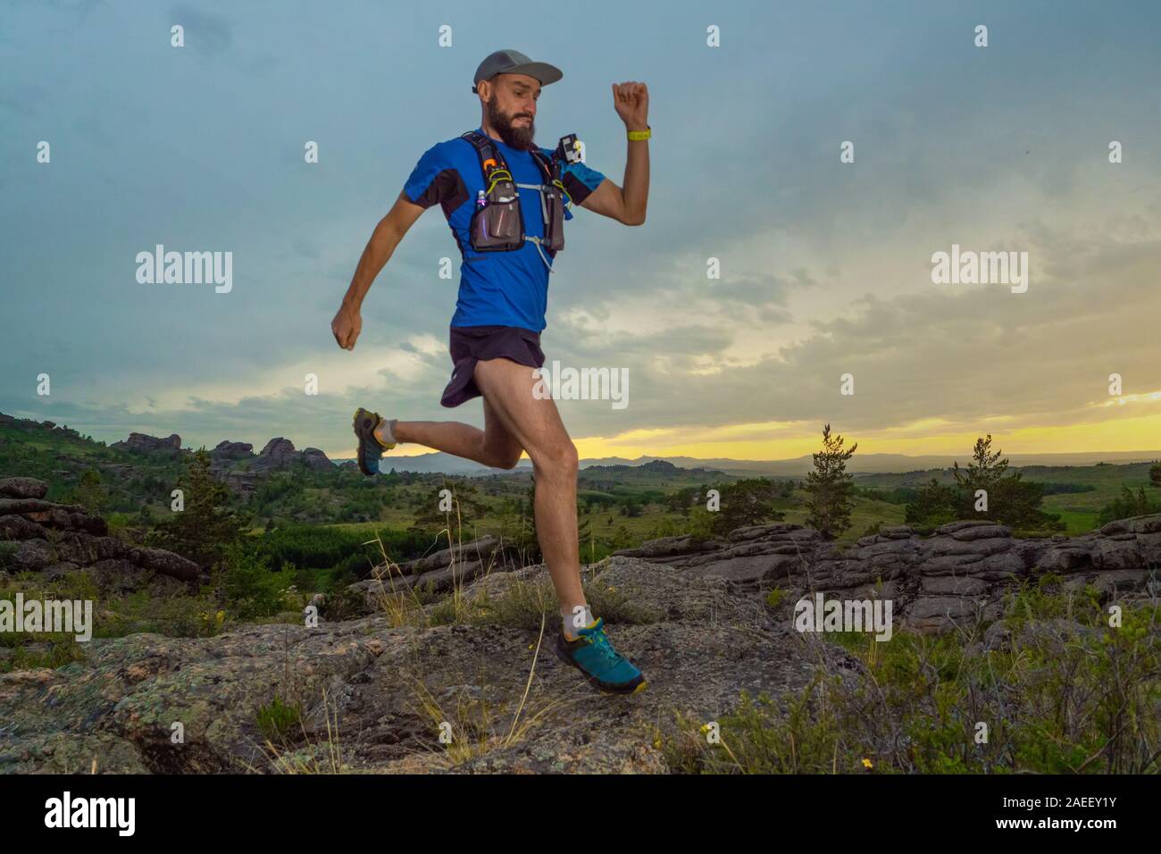 Eine männliche Läufer verläuft entlang einer Mountain Trail. Mann in einem blauen Pullover und in schwarzen Shorts. Das Training im Freien am Abend. Stockfoto