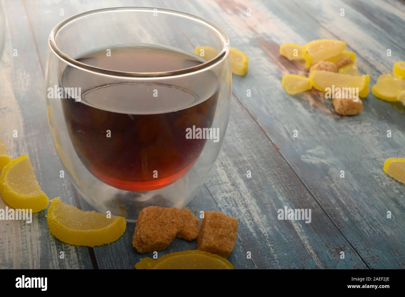 Marmelade Zitronenscheiben, Stücke von braunem Zucker und einem Glas schwarzen Tee auf einem hölzernen Hintergrund. Süße Nachspeise. Nahaufnahme Stockfoto