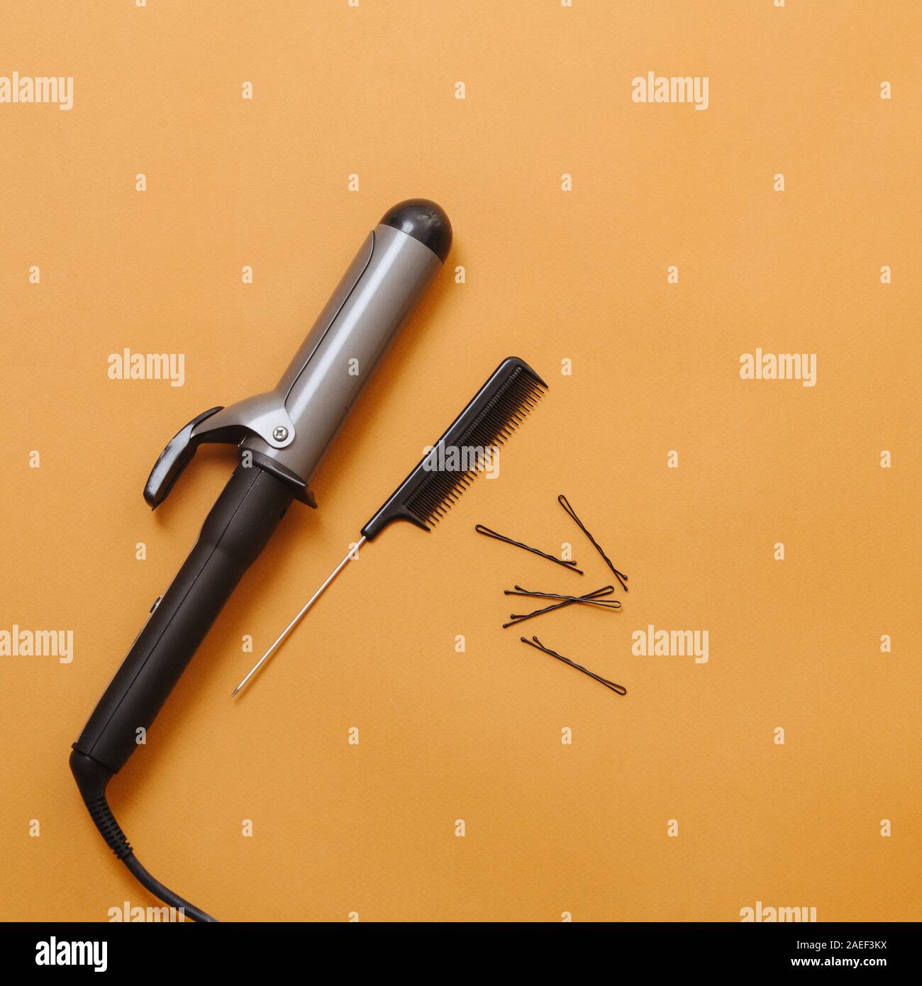 Friseur Tools: Lockenstab, rattenschwanz Kamm, bobby Pins über Orange. Ansicht von oben Stockfoto