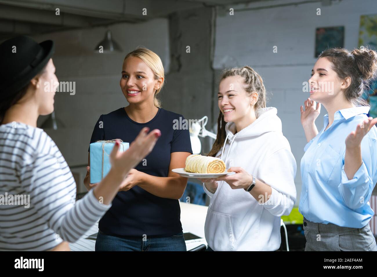 Drei fröhliche junge Frauen gratulieren Ihrer Kollegin zu ihrem Geburtstag Stockfoto