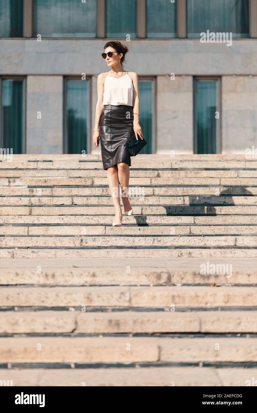 Modische brunette Geschäftsfrau in einem braunen Bleistiftrock aus Leder und cremefarbene Seidenbluse, Sonnenbrillen zu Fuß auf der Straße, auf Treppen Stockfoto
