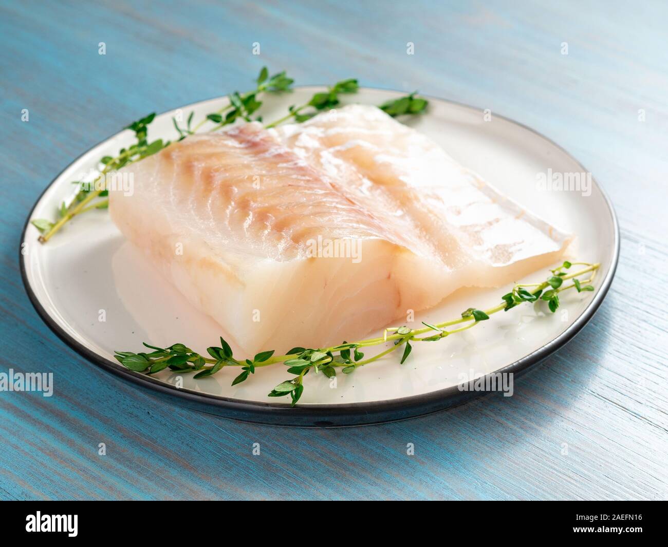 Stück raw cod Fischfilet auf Platte auf Blau Holztisch, Seitenansicht Stockfoto