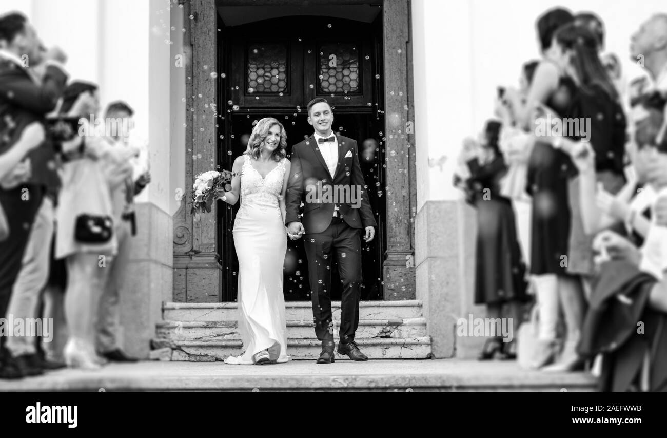 Brautpaar Verlassen der Kirche nach der Trauung, Familie und Freunde feiern ihre Liebe mit der Dusche der Seifenblasen, benutzerdefinierte untergraben. Stockfoto