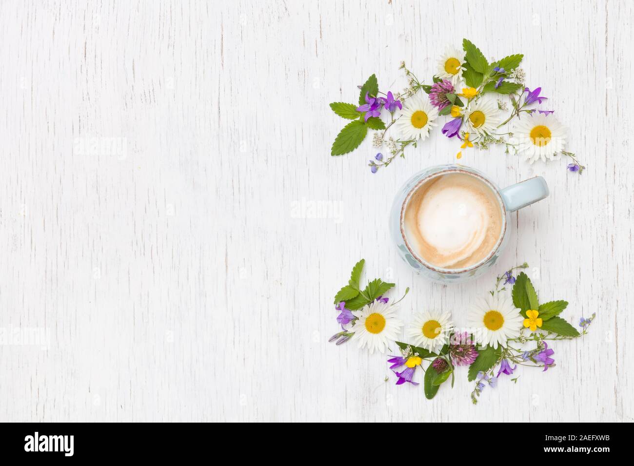 Ansicht von oben auf die schönen wilden Blumen in Form von Kranz und einer Tasse Cappuccino auf weißem Holz- Hintergrund. Sommer Blumen, Blätter, Blüten und Co Stockfoto