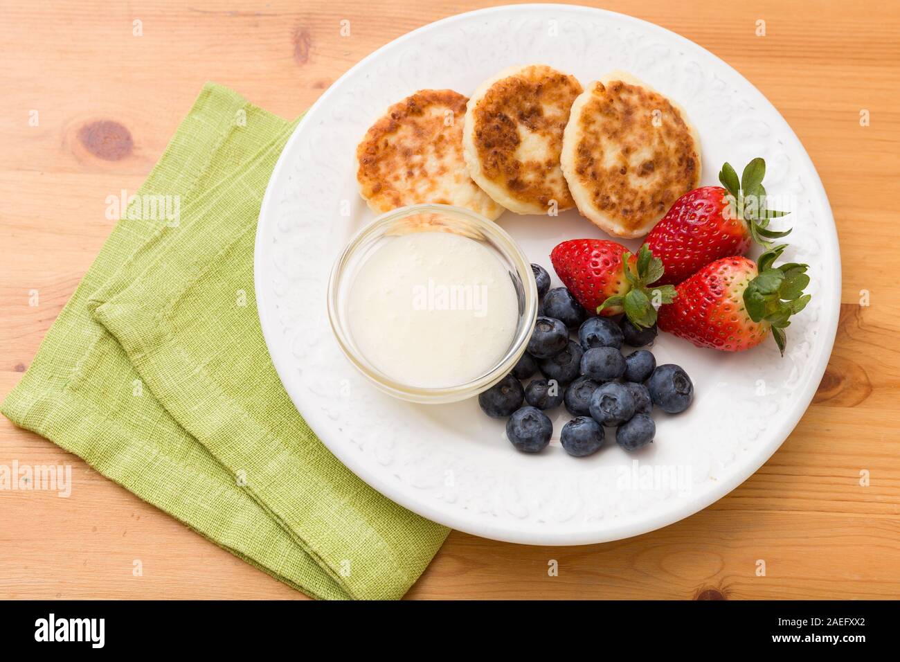 Ansicht von oben auf die weiße Platte mit Kuchen von Hüttenkäse mit Heidelbeeren, Erdbeeren und süßen Sause auf hölzernen Tisch. Gesunden Snack. Frühstück ide Stockfoto
