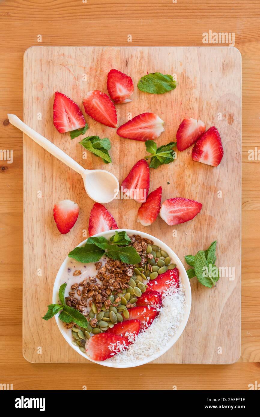 Frühstück Berry Smoothie Schüssel gekrönt mit Erdbeere, Kürbiskerne, Kokos, Müsli und frischer Minze. Strawberry Banana Smoothie Schüssel. Gesunde Breakfas Stockfoto