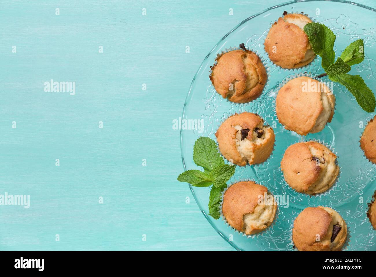 Leckere hausgemachte Vanille Muffins mit Schokolade und Minze auf der Glasplatte auf Türkisfarbenem Hintergrund. Süße Nachspeise für Feier, Party oder einen Snack. Stockfoto