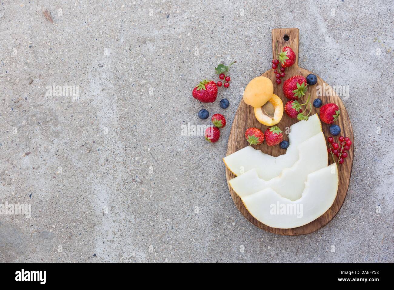 Draufsicht auf Holzbrett mit frischem Obst und Beeren: Melone, Erdbeeren, Blaubeeren, Apricot und Rot aktuelle auf konkreten Hintergrund. Gesundheit Stockfoto