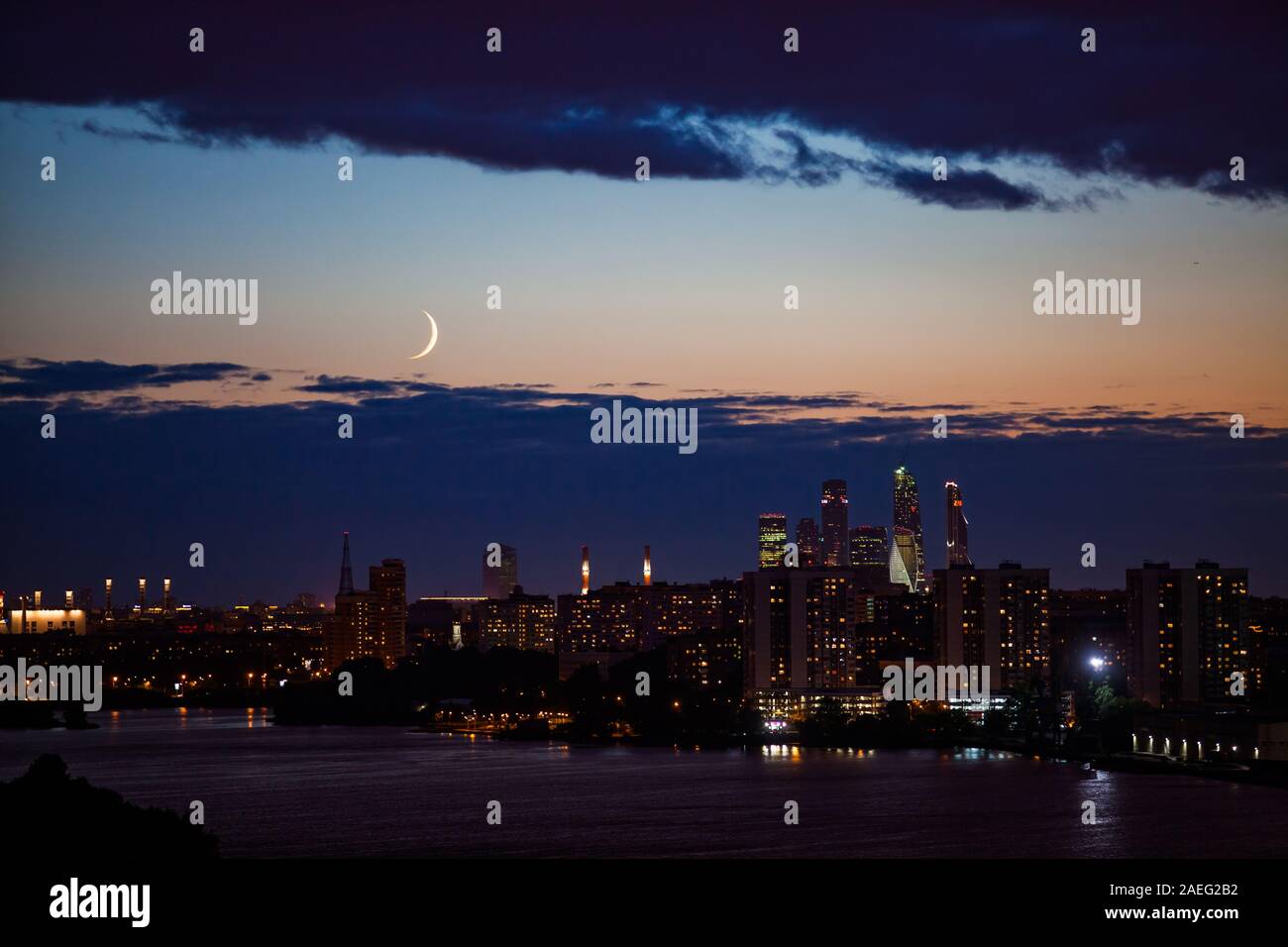 Nachts oder abends Stadtbild mit Wolkenkratzern und Stadt Silhouette am Fluss in tiefem Blau und Gelb Himmel mit Wolken und Crescent. Stockfoto