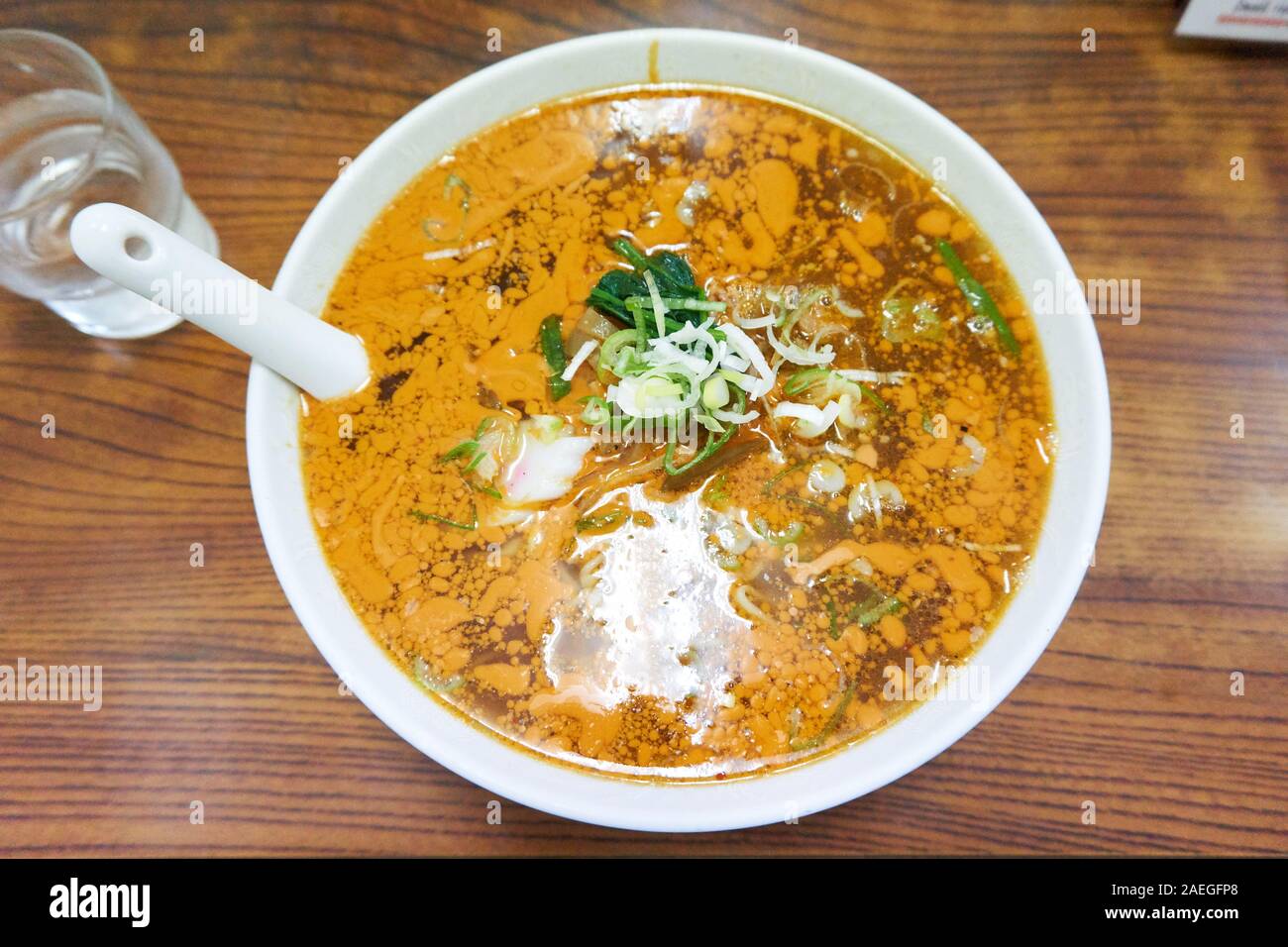 Auf einem Holztisch sitzt eine heiße Schüssel mit japanischen Bräunungsmännern (Ramen) mit grünen Zwiebelscheiben darauf. Stockfoto