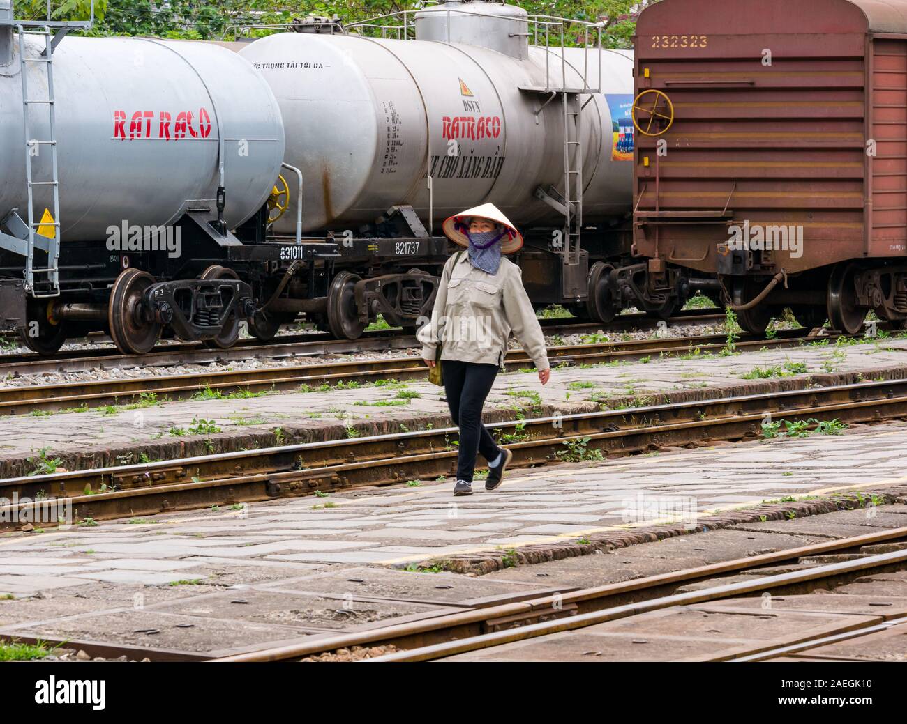 Vietnamesische Frau mit konischen Hut gehen auf Gleisen mit Güterzügen, Hanoi, Vietnam, Asien Stockfoto