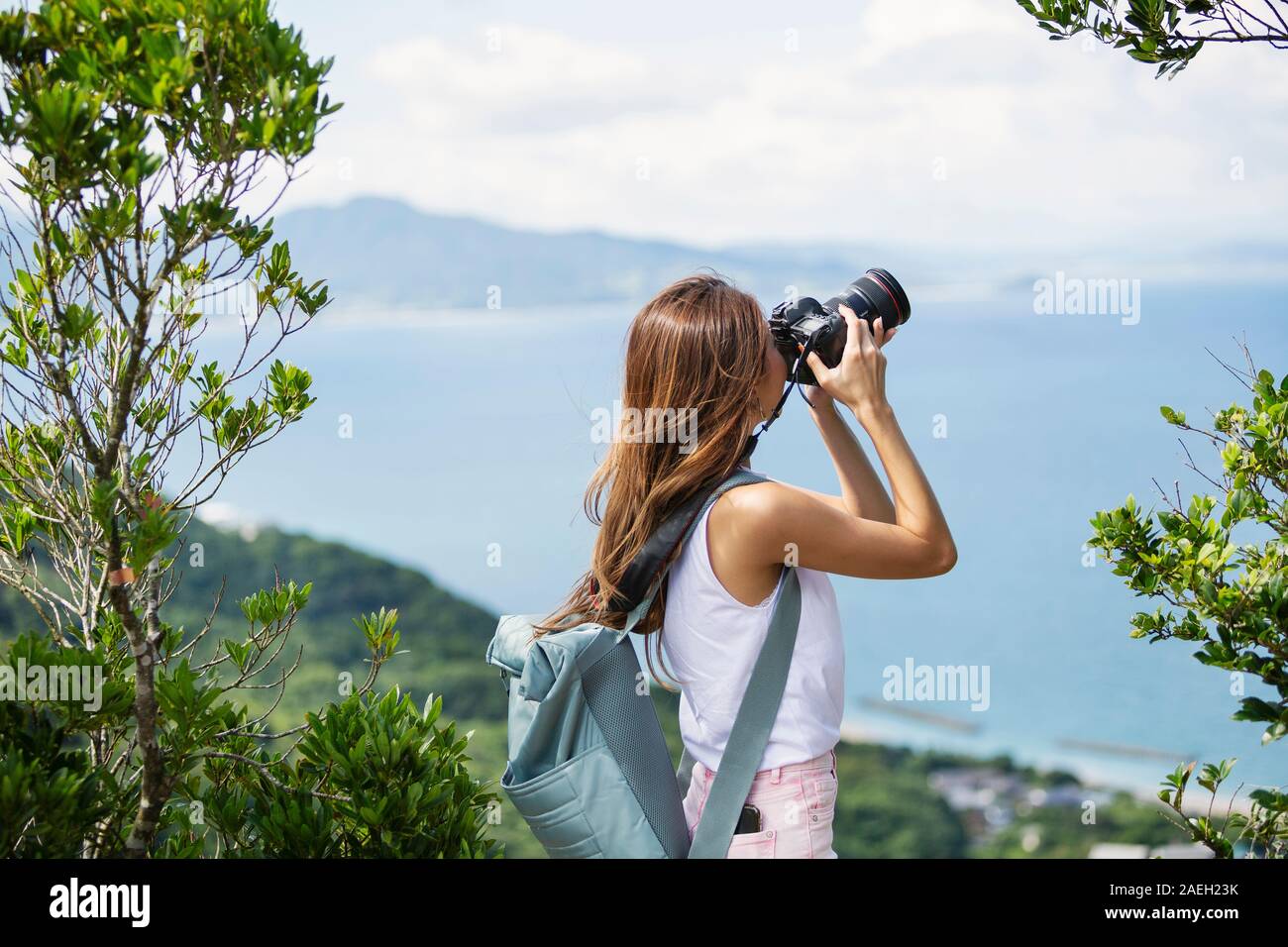 Japanische Frau, die Rucksack machen Fotos auf einer Klippe, auf das Meer im Hintergrund. Stockfoto