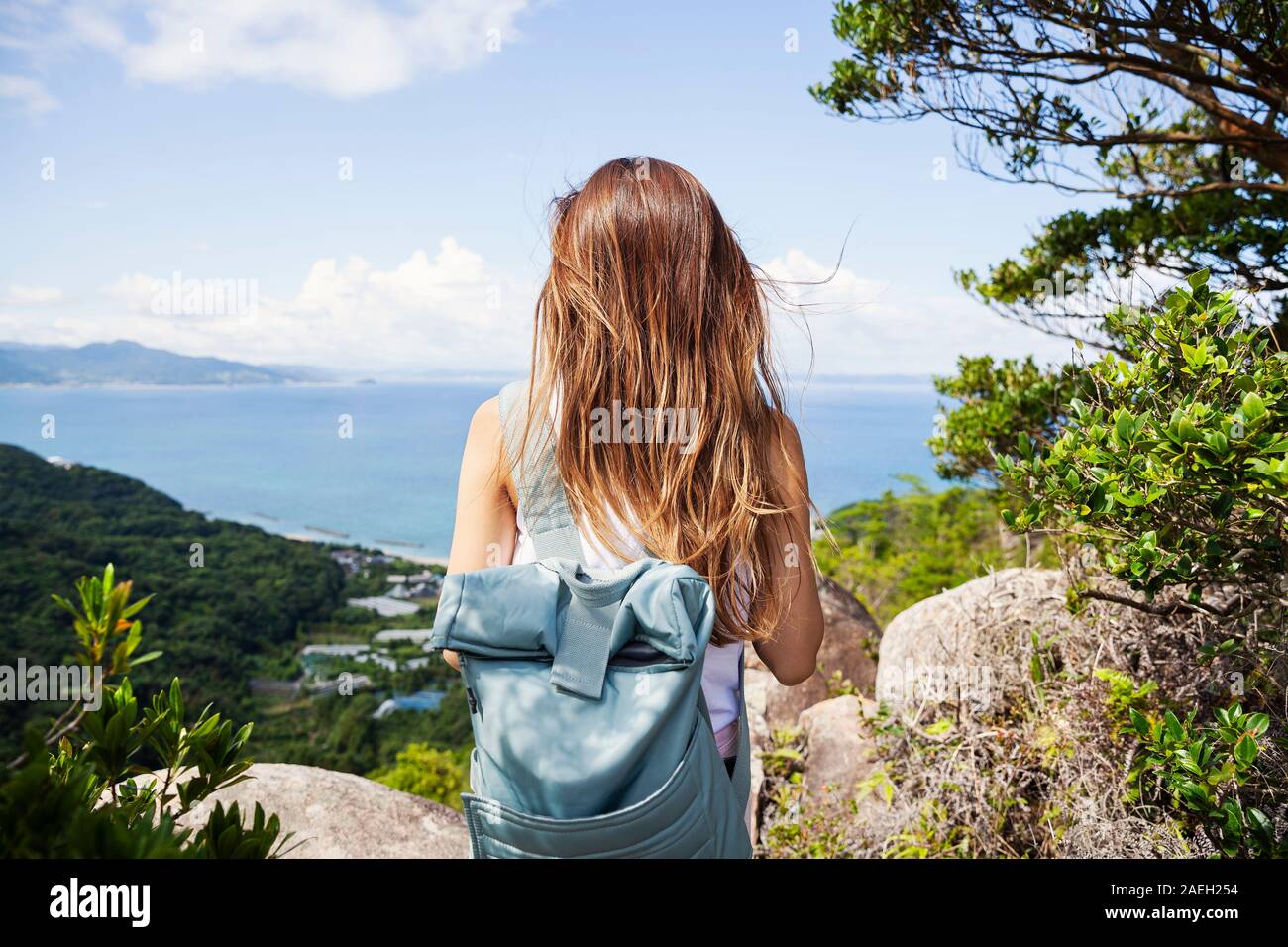 Ansicht der Rückseite Frau Rucksack tragen steht auf einem Felsen, Felsen, das Meer im Hintergrund. Stockfoto