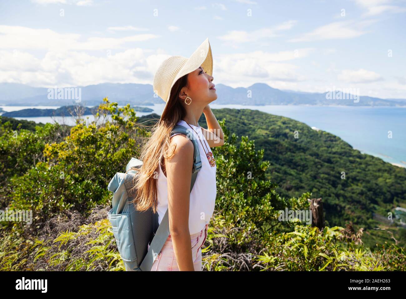 Japanische Frau mit Hut und der Rucksack steht auf einer Klippe, auf das Meer im Hintergrund. Stockfoto
