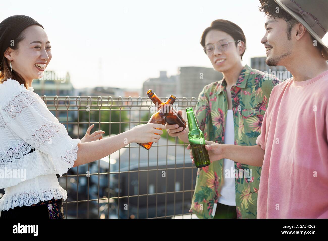 Junge Japaner, Männer und Frau, die auf einem Dach in einem urbanen Umfeld, trinken Bier. Stockfoto