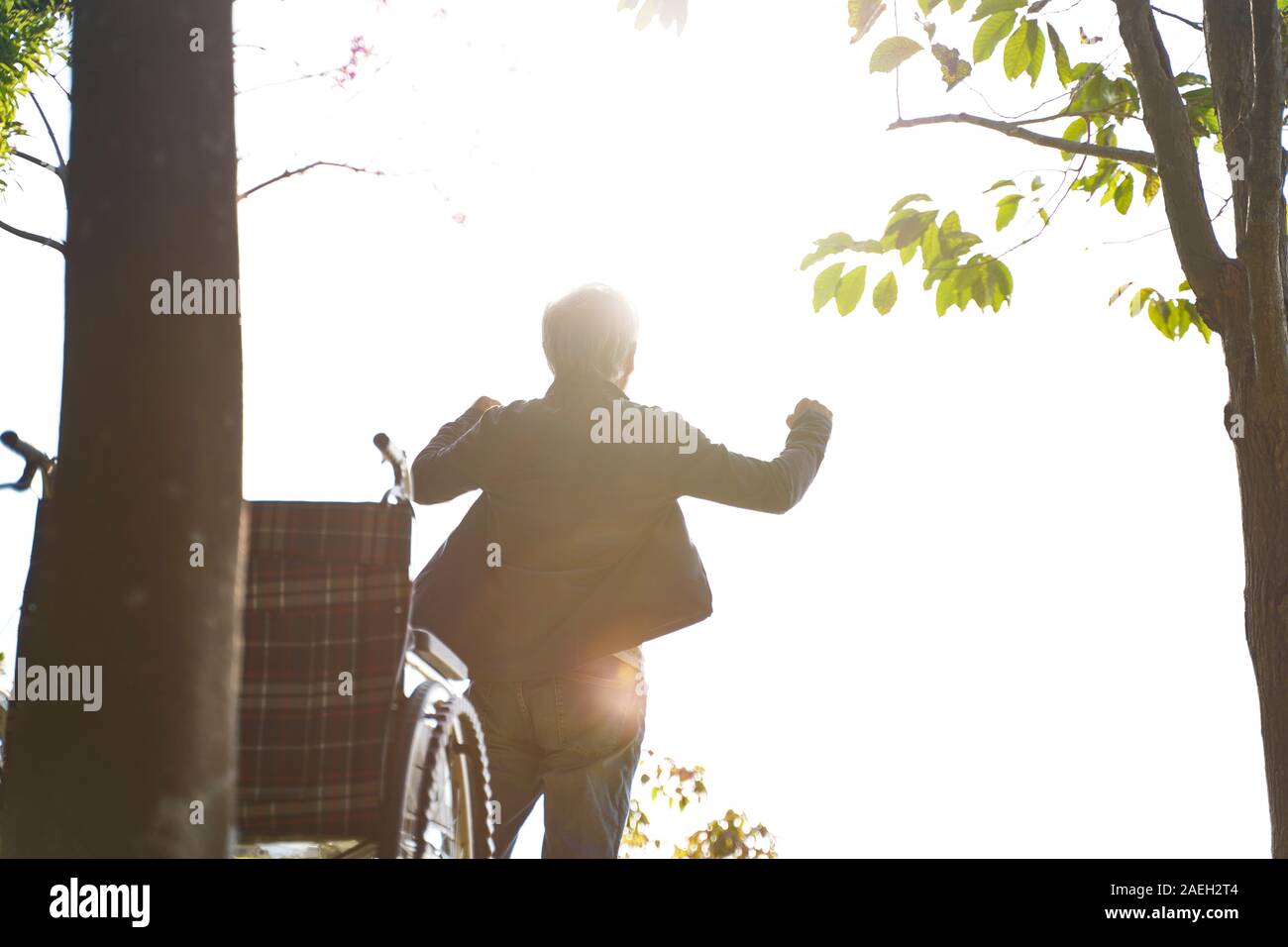 Ansicht der Rückseite des asiatischen älterer Mann stand für Rollstuhlfahrer mit offenen Armen Stockfoto