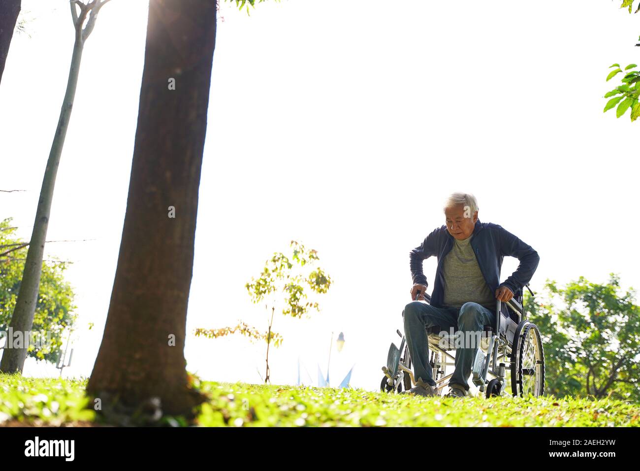 Senior asiatischer Mann versucht, vom Rollstuhl im Freien zu erhalten Stockfoto