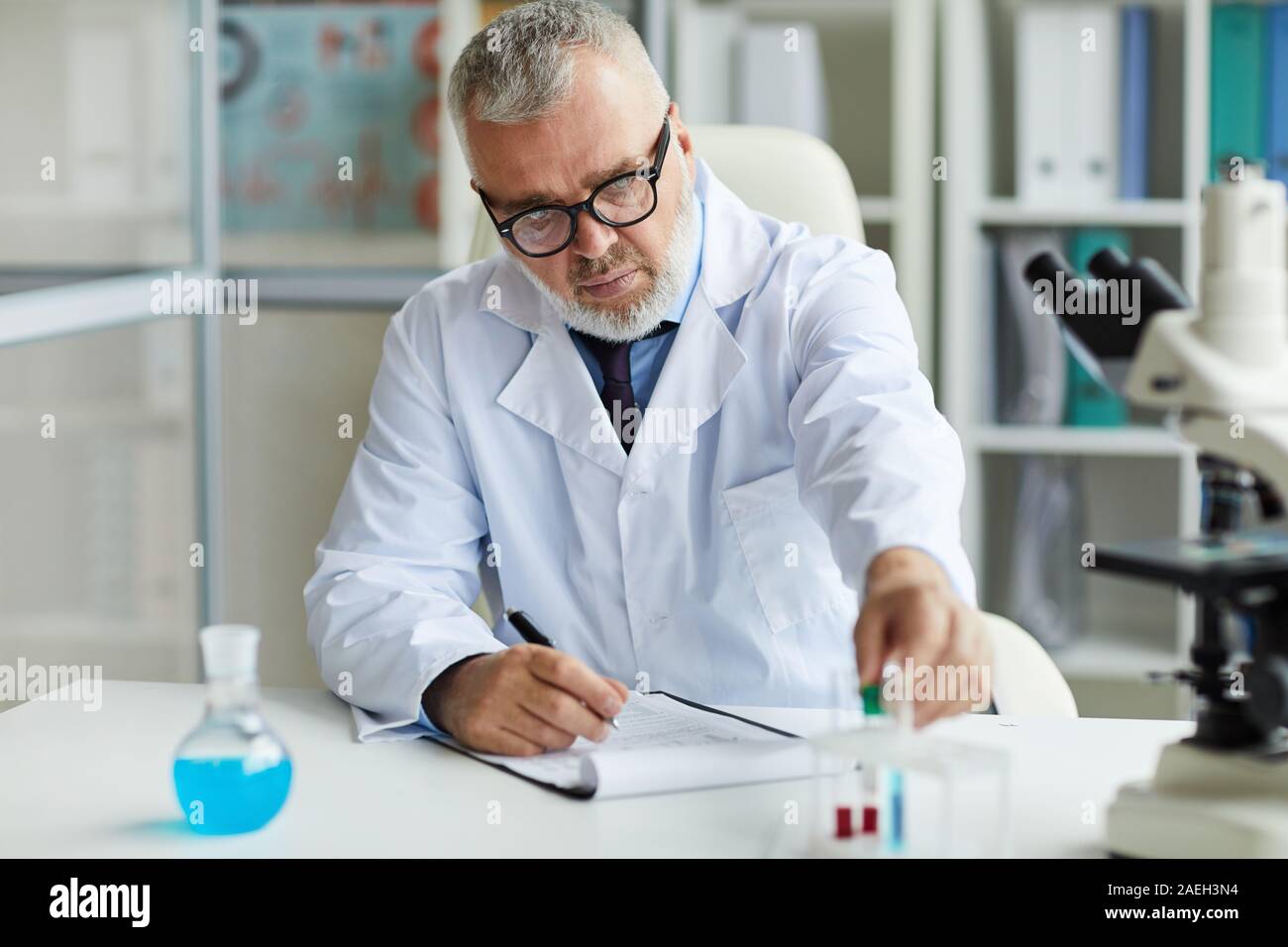 Reifen Wissenschaftler in Brillen an seinem Arbeitsplatz mit Proben und Dokumente im Labor arbeiten Stockfoto