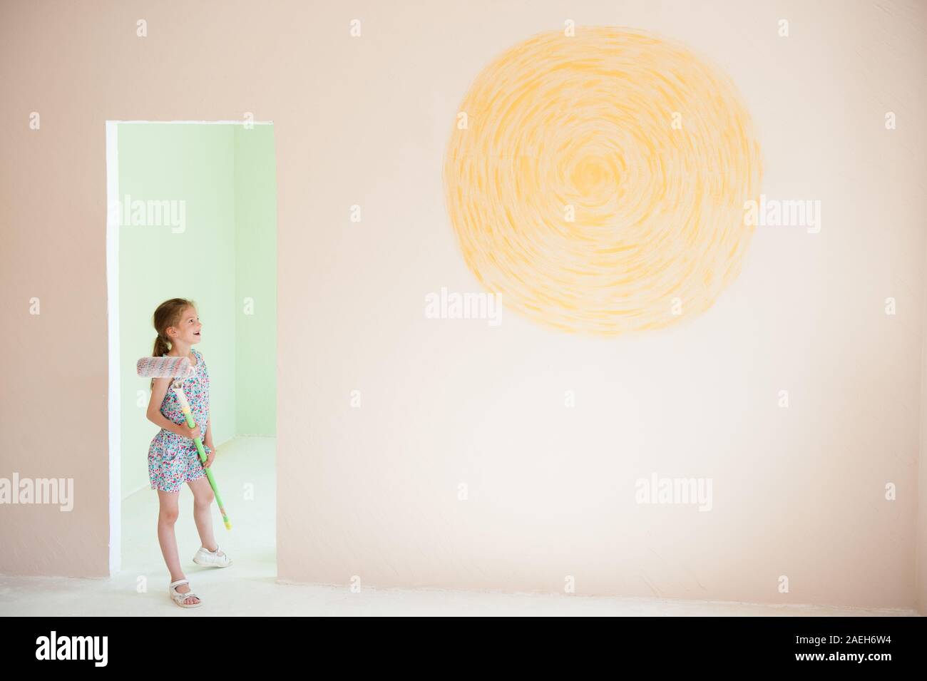 Happy little Girl holding Malerei Walze drinnen neue Raumgestaltung mit gelben Sonne an der Wand Stockfoto