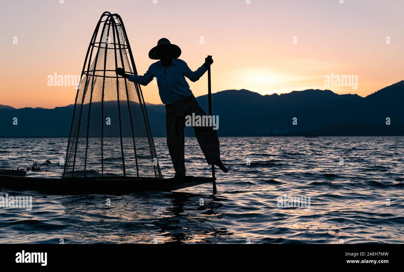 Die burmesische Fischer für Touristen bei Sonnenuntergang posiert am Inle See. Die traditionelle Fischernetze hält er nicht mehr für den Fischfang der Intha verwendet. Stockfoto