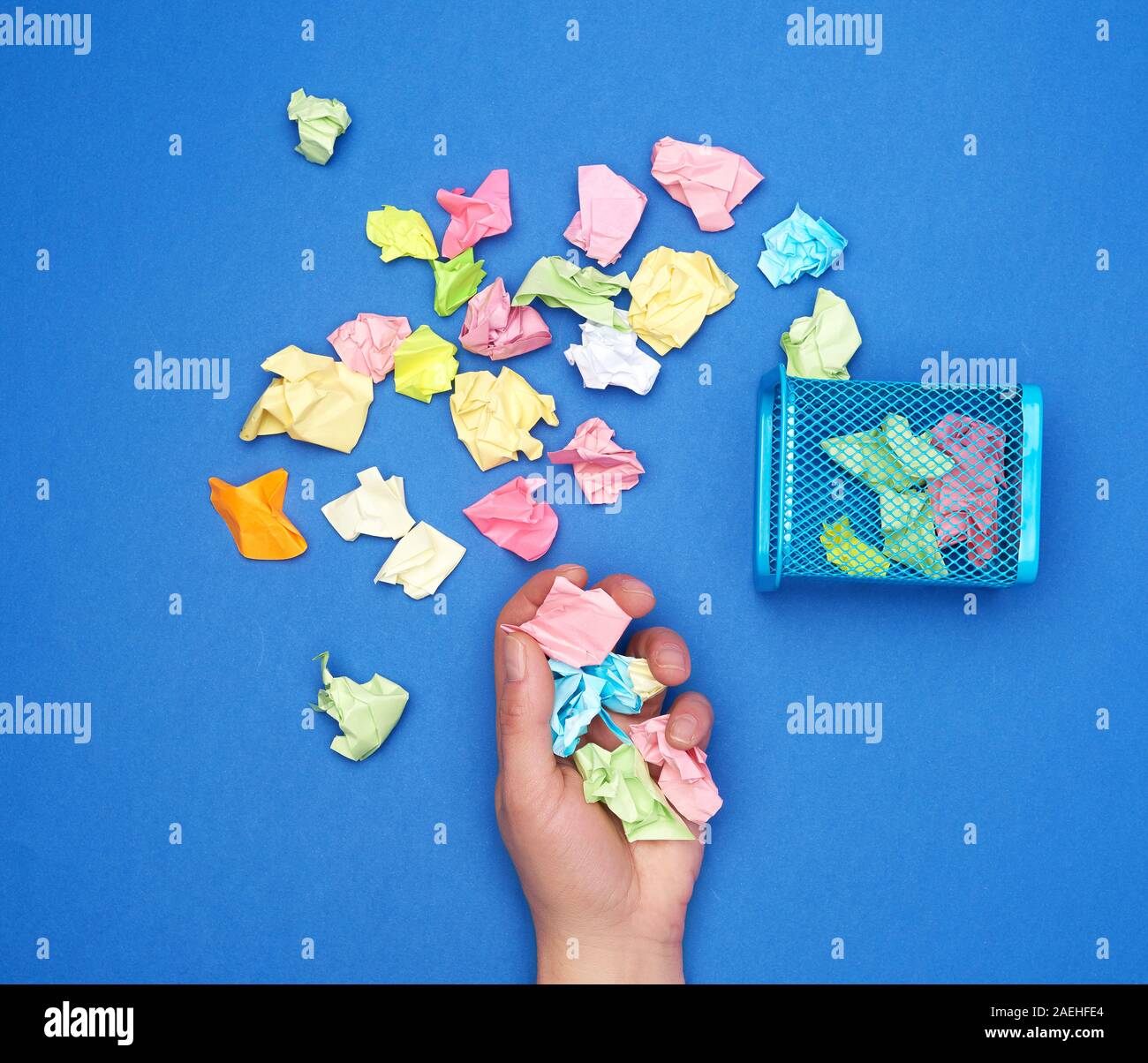 Weibliche Hand hält ein Haufen zerknüllter mehrfarbige Stück Papier, neben einem Metall Mülleimer, Stockfoto
