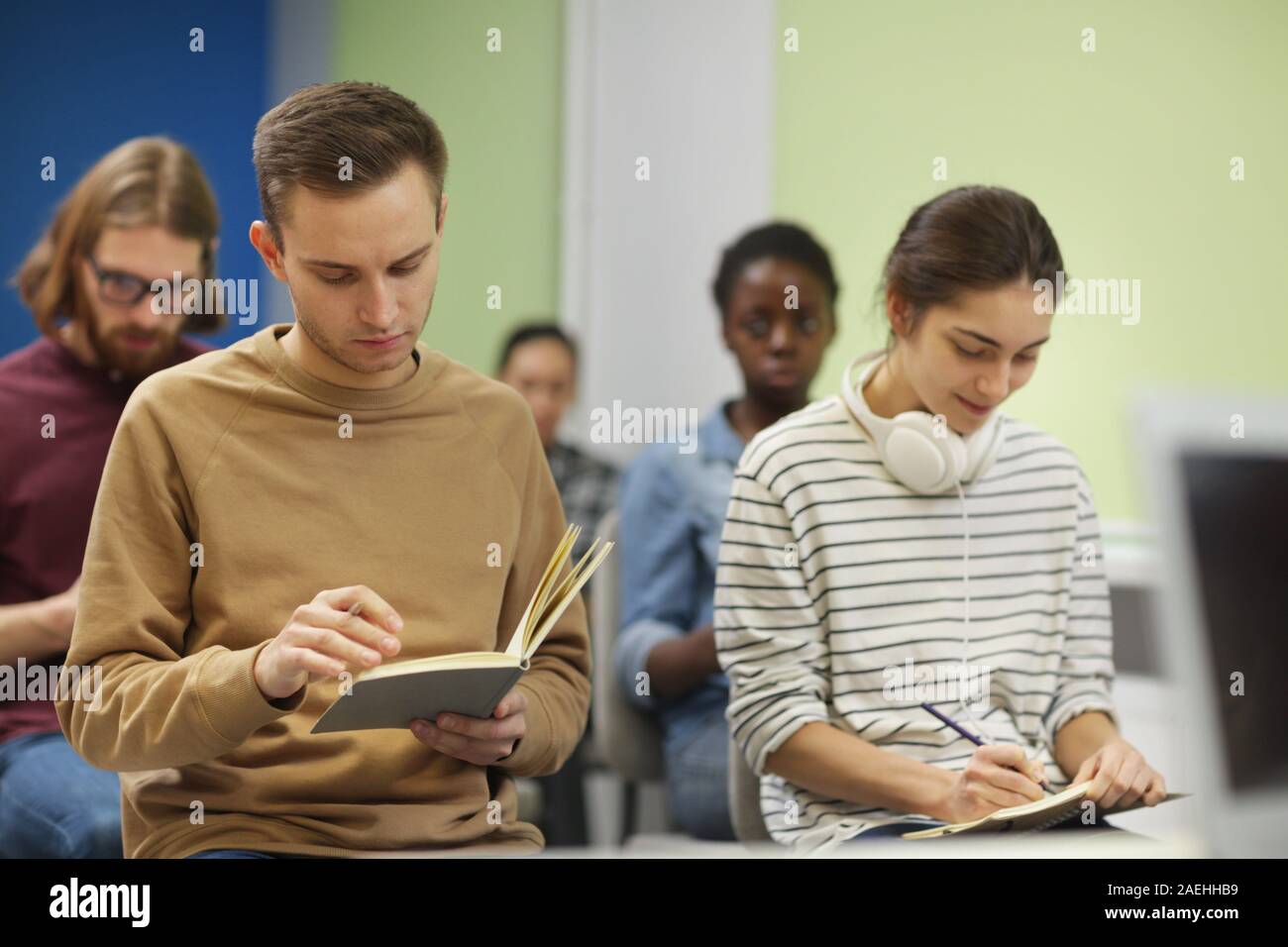 Junge Menschen in Freizeitkleidung sitzen auf Stühlen und Notizen in Notebooks während des Seminars Stockfoto