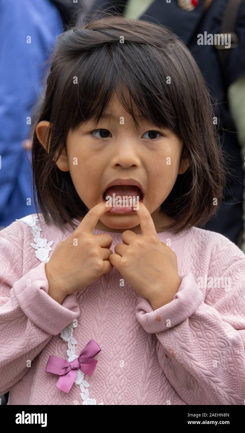 Japanische Mädchen ein Gesicht von ihrem Mund ziehen, Tokio, Japan Stockfoto