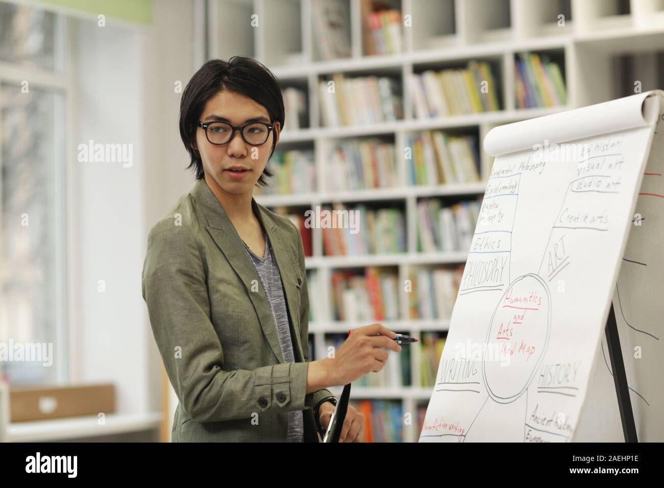 Portrait von Asiatischen jungen Mann in Brillen stehen in der Nähe der Tafel, und wenn man die Kamera während einer Präsentation Stockfoto