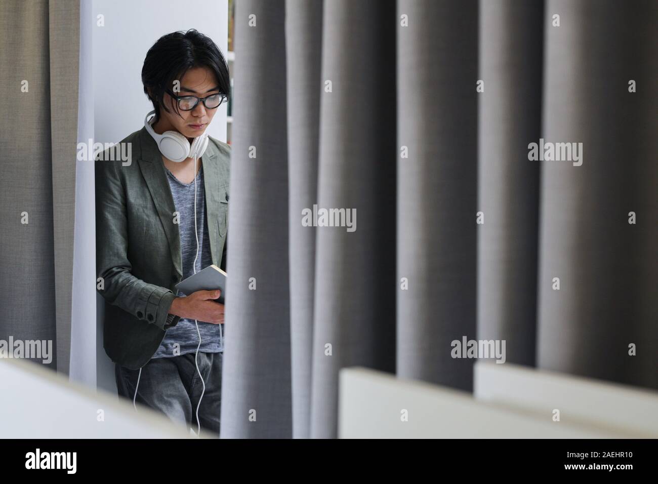 Asiatische junge Mann in Brillen und mit Kopfhörern besetzt ein Buch lesen Stockfoto