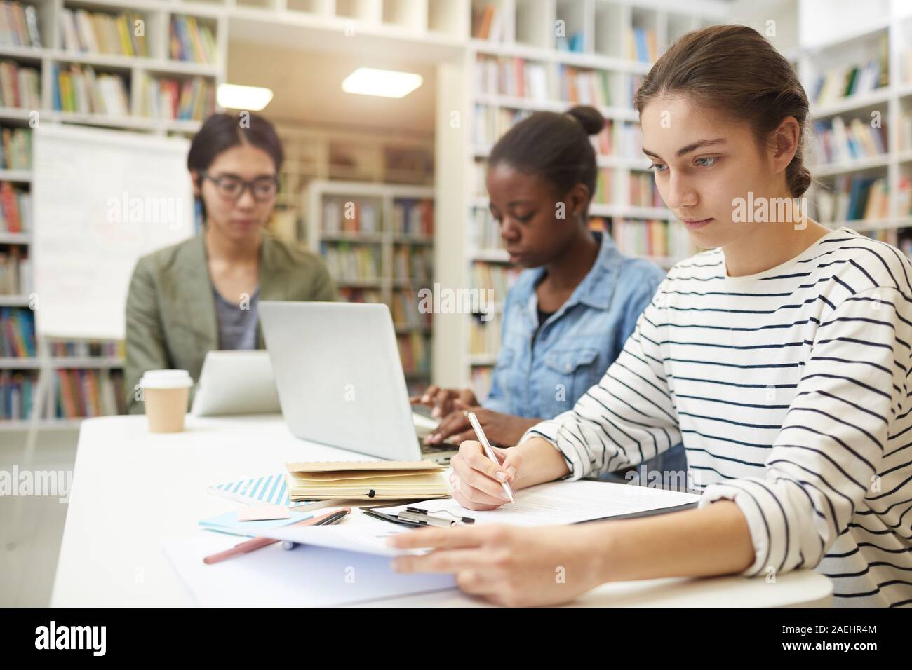 Junge Frau am Tisch sitzen und arbeiten mit Papieren, die Sie für Prüfungen gemeinsam mit Ihren Freunden im Hintergrund Stockfoto