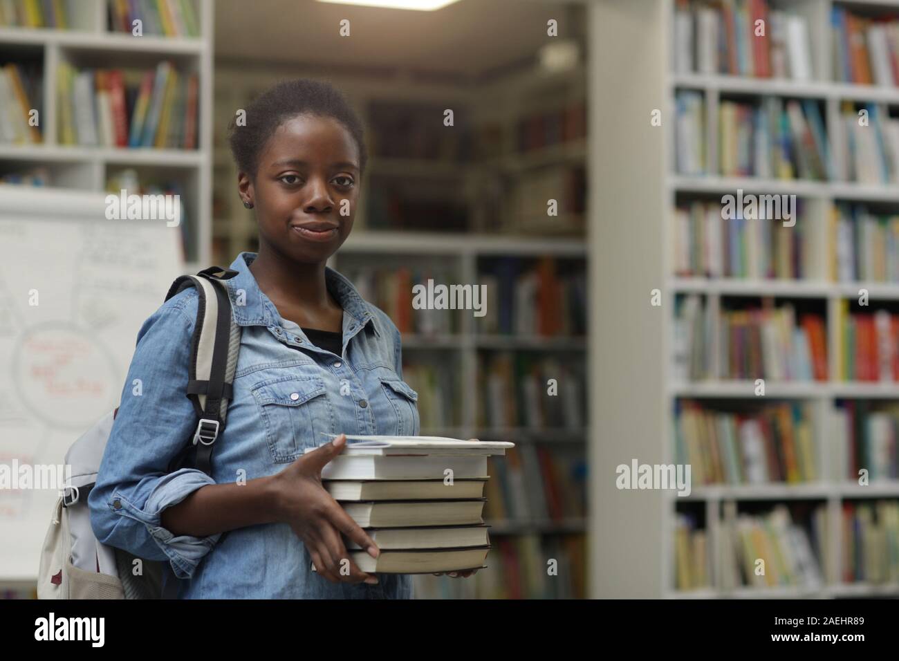 Porträt der Afrikanische junge Frau mit Blick auf die Kamera halten Haufen Bücher in ihren Händen in der Bibliothek Stockfoto