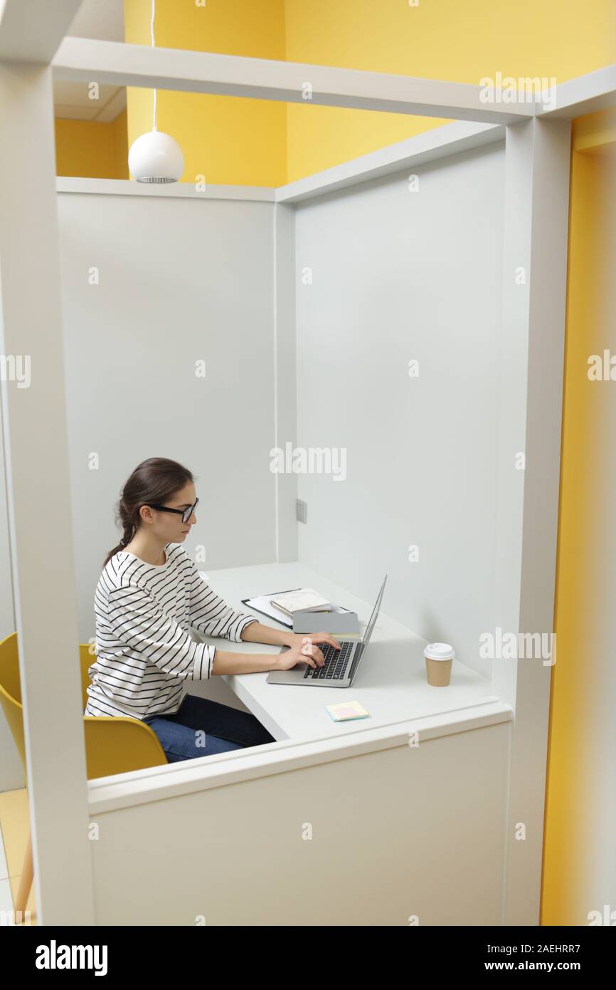 Junge Geschäftsfrau in Brillen und legere Kleidung sitzen an Ihrem Arbeitsplatz und Arbeiten am Laptop im Büro Stockfoto