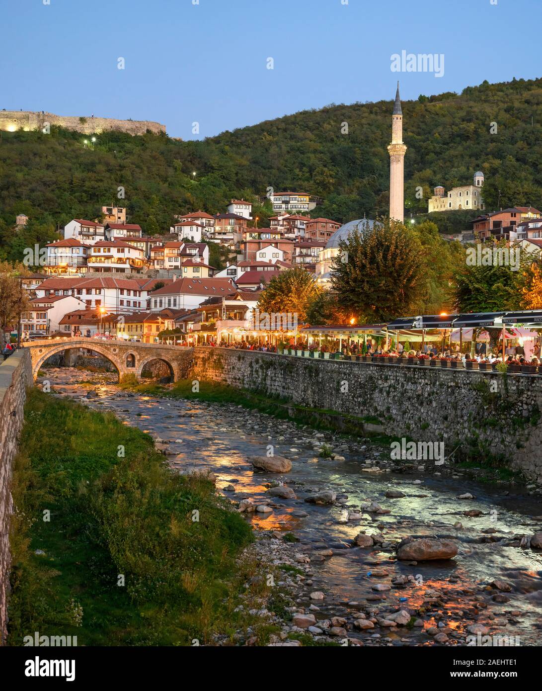 Cafés und Restaurants, die von der Seite e des Bistrica Fluss mit der Altstadt von Prizren und der Sinan Pascha Moschee im Hintergrund. Prizren, Kosovo, Stockfoto