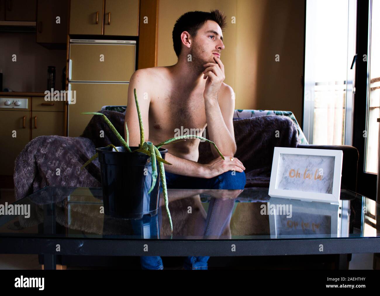 Ein intelligenter junger Mann sitzt auf einem Sofa ohne ein Hemd am Fenster suchen Stockfoto