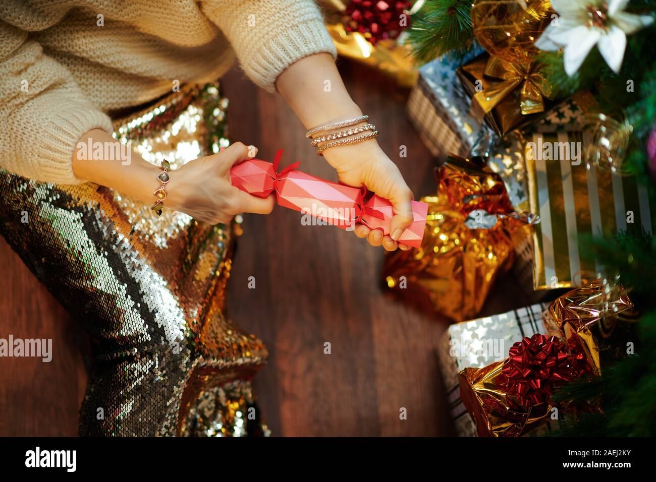 Nahaufnahme auf elegante Frau in Gold Pailletten Rock und weißen Pullover unter dem geschmückten Weihnachtsbaum in der Nähe des heutigen Boxen reißen Victorian Christmas Cracker. Stockfoto
