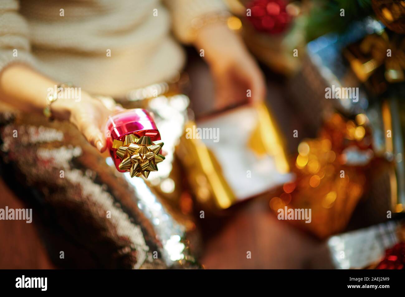 Nahaufnahme auf stilvolle Frau mittleren Alters in Gold Pailletten Rock und weißen Pullover unter dem geschmückten Weihnachtsbaum in der Nähe des heutigen Boxen Betrieb vorhanden und f Stockfoto