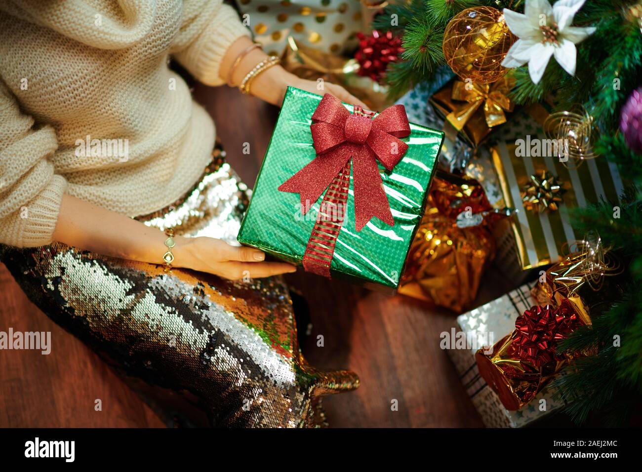 Nahaufnahme auf junge Frau in Gold Pailletten Rock und weißen Pullover unter dem geschmückten Weihnachtsbaum in der Nähe des heutigen Boxen übersicht Weihnachtsgeschenk. Stockfoto