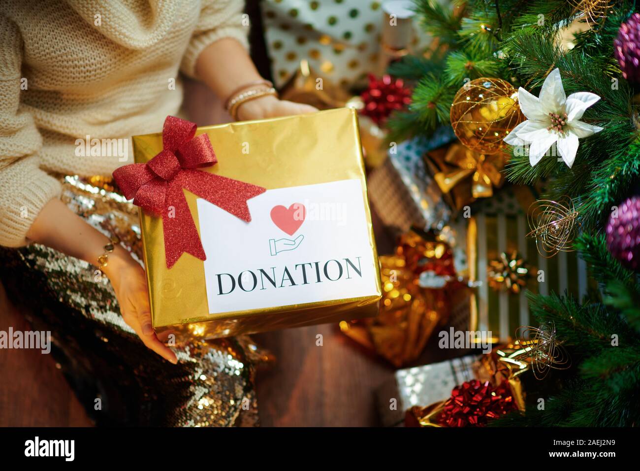 Nahaufnahme auf elegante mittleren Alter Hausfrau in Gold Pailletten Rock und weißen Pullover unter dem geschmückten Weihnachtsbaum in der Nähe des heutigen Boxen halten spezielle Chris Stockfoto