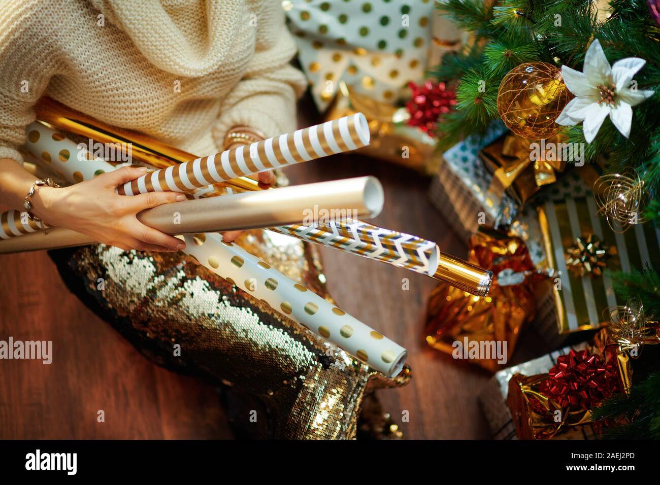 Nahaufnahme auf elegante 40-jährige Frau in Gold Pailletten Rock und weißen Pullover unter dem geschmückten Weihnachtsbaum in der Nähe des heutigen Boxen holding Geschenkpapier r Stockfoto