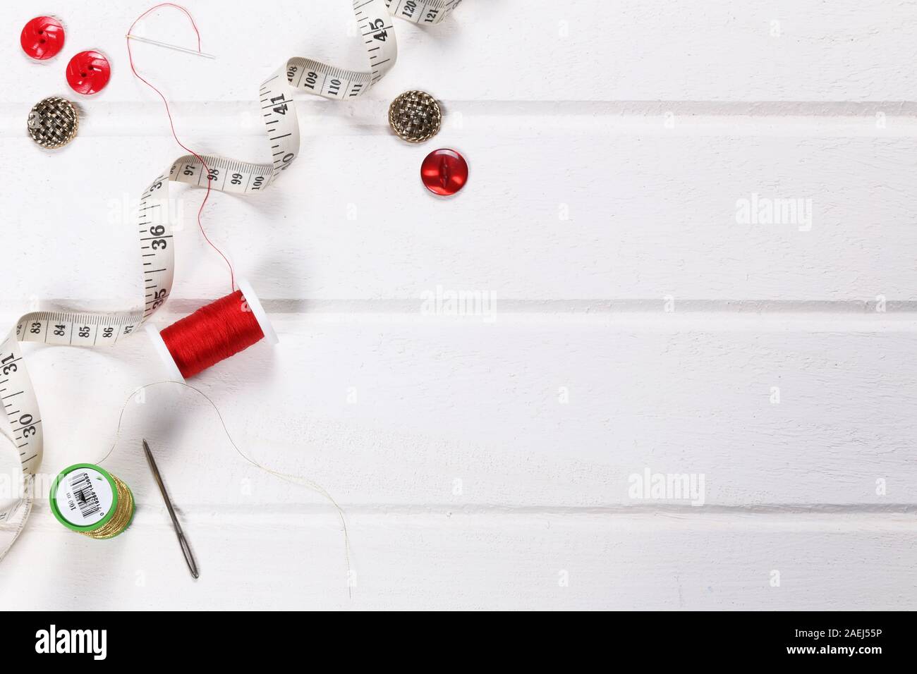 Flaches Nähzeug mit Baumwollrollen, Knöpfen und Maßband auf weißem Hintergrund mit Platz für Text oder Design rot-goldene Farben Stockfoto