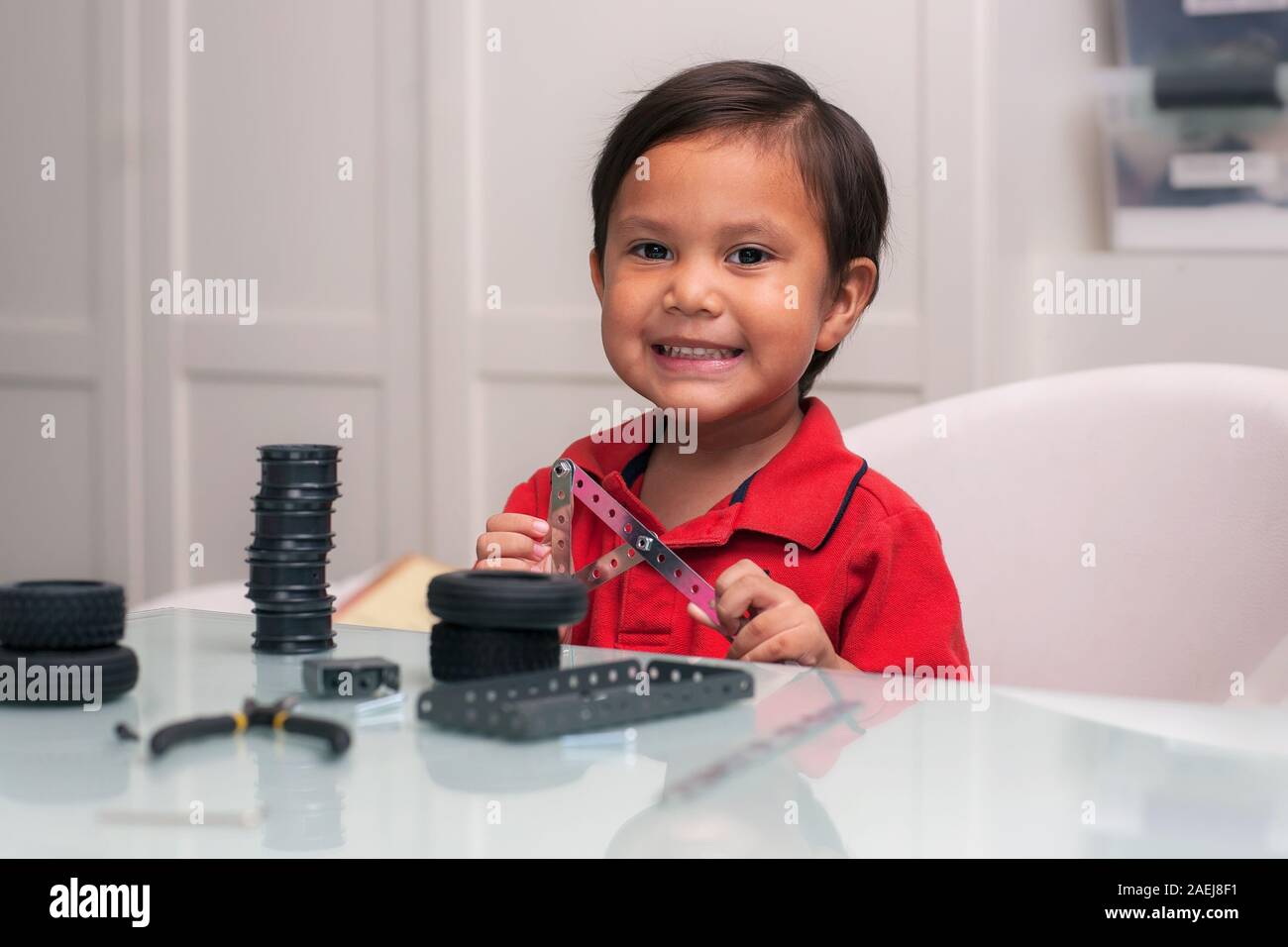 Eine intelligente junge Zicklein, das Lächeln und das Sitzen mit einem Glas Schreibtisch, halten die montierten Teile von ein Spielzeugauto. Stockfoto