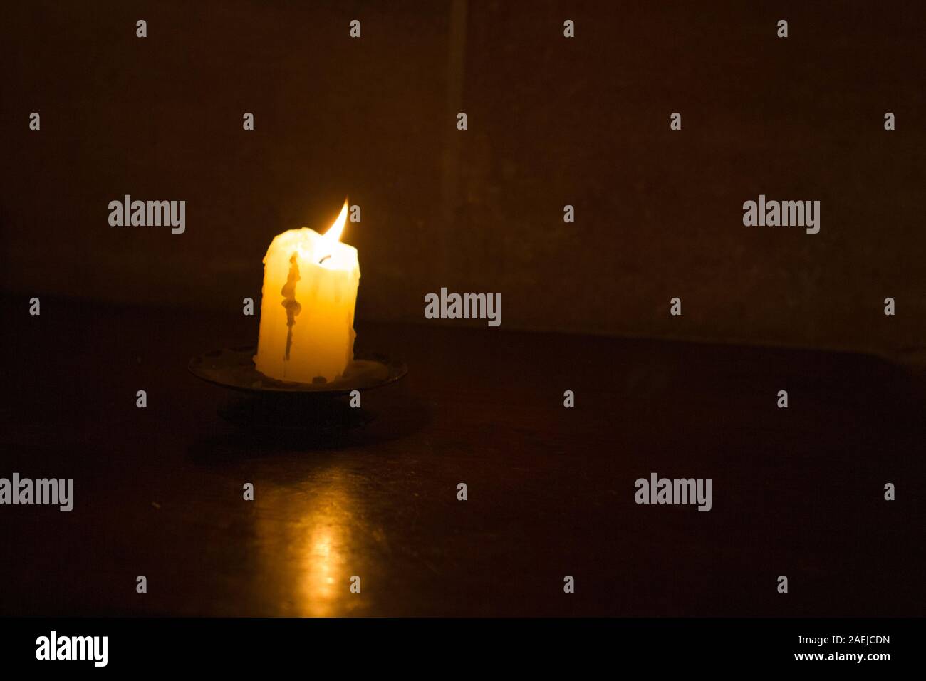 Eine brennende Kerze in einer Kirche gegen die Dunkelheit und einer dunklen Mauer als Symbol für den Glauben, die Religion, das Christentum isoliert Stockfoto
